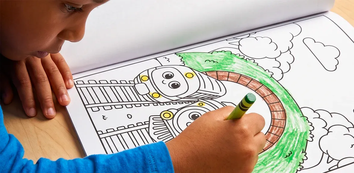 A boy coloring a train page with a green crayon